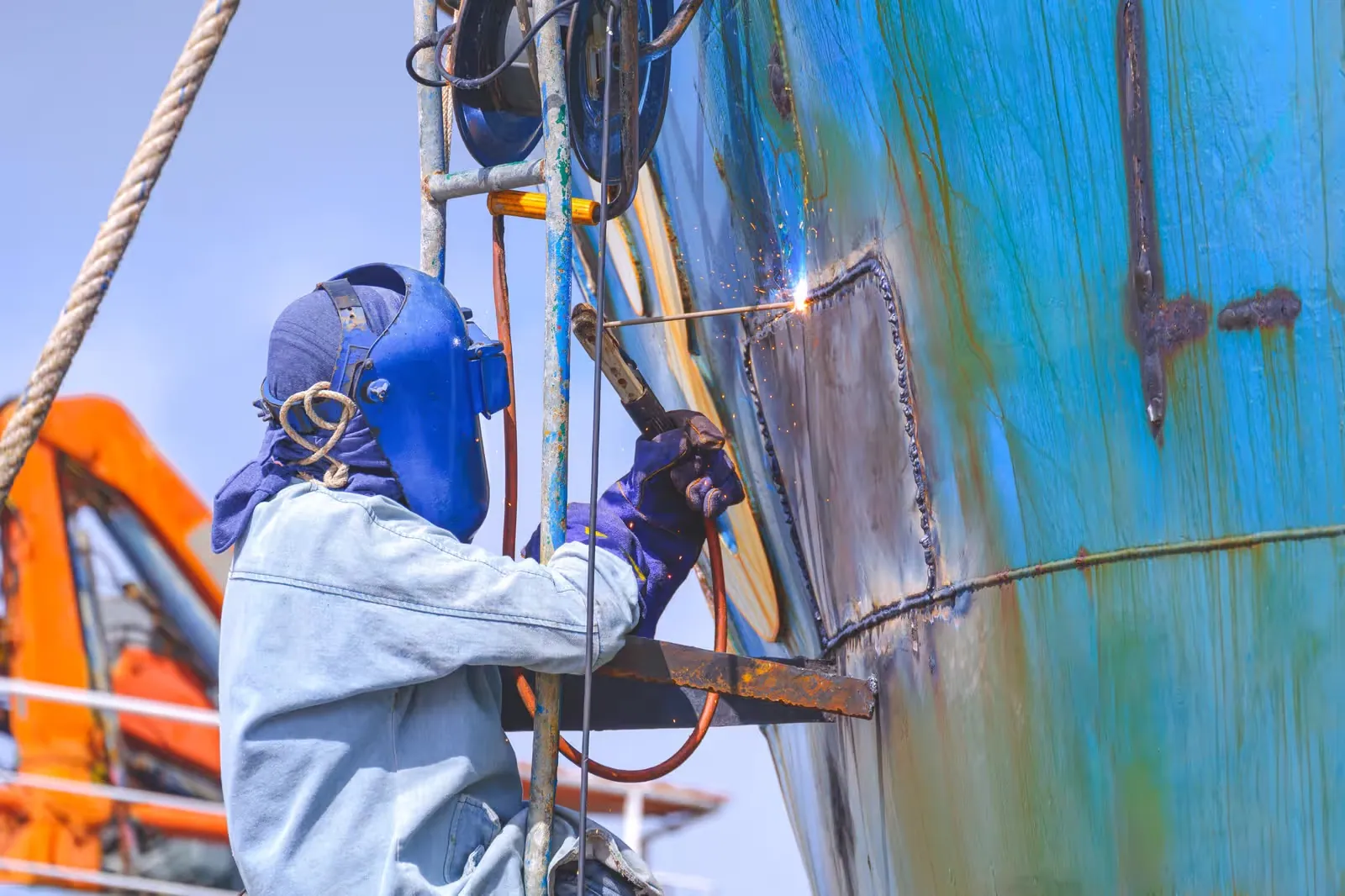 Welder fabricating a hull patch on a vessel